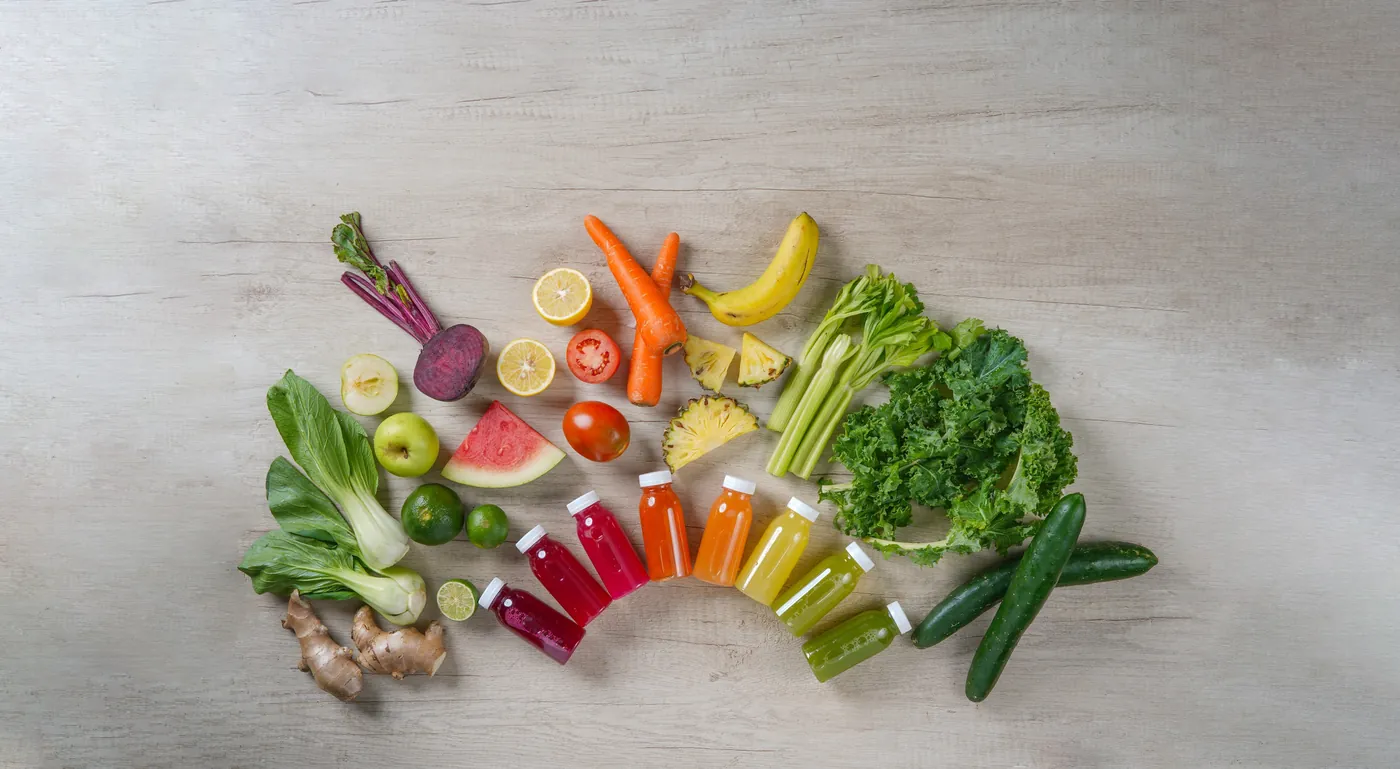 Sayur, buah, dan botol jus Kboon tersusun melengkung di atas meja batu